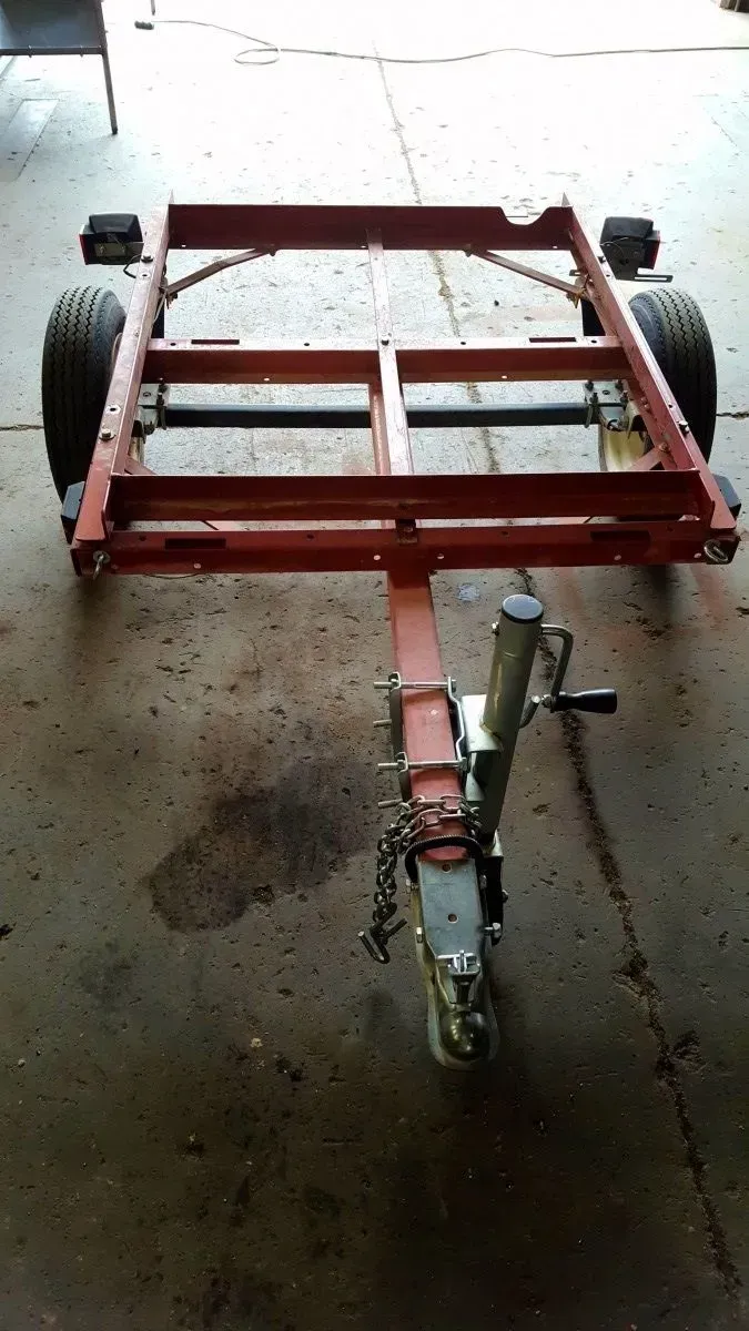 Red metal utility trailer with two large wheels and a front hitch, parked on a concrete floor.
