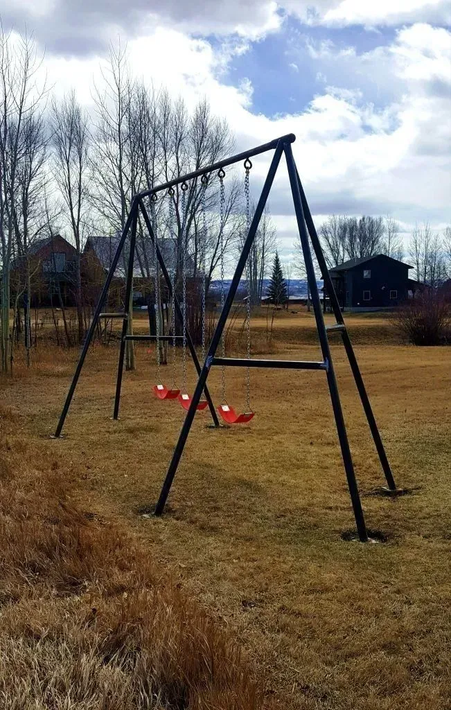 Empty playground swing set in a grassy field under a cloudy sky