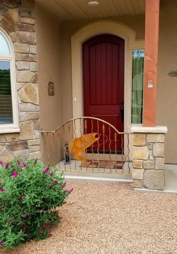 Front entrance with a red door, stone facade, and small curved railing beside a gravel walkway.
