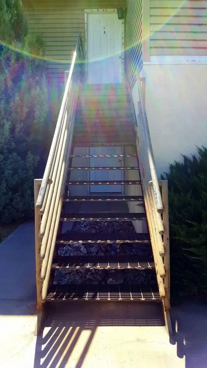 Outdoor staircase with white railings leading up to a building, lit by bright sunlight.