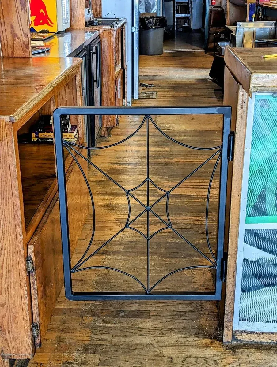 Open decorative metal gate blocking a narrow wooden aisle in a rustic interior.