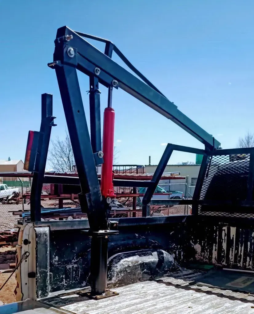 Industrial crane arm with red hydraulic cylinders mounted on a truck bed under a blue sky