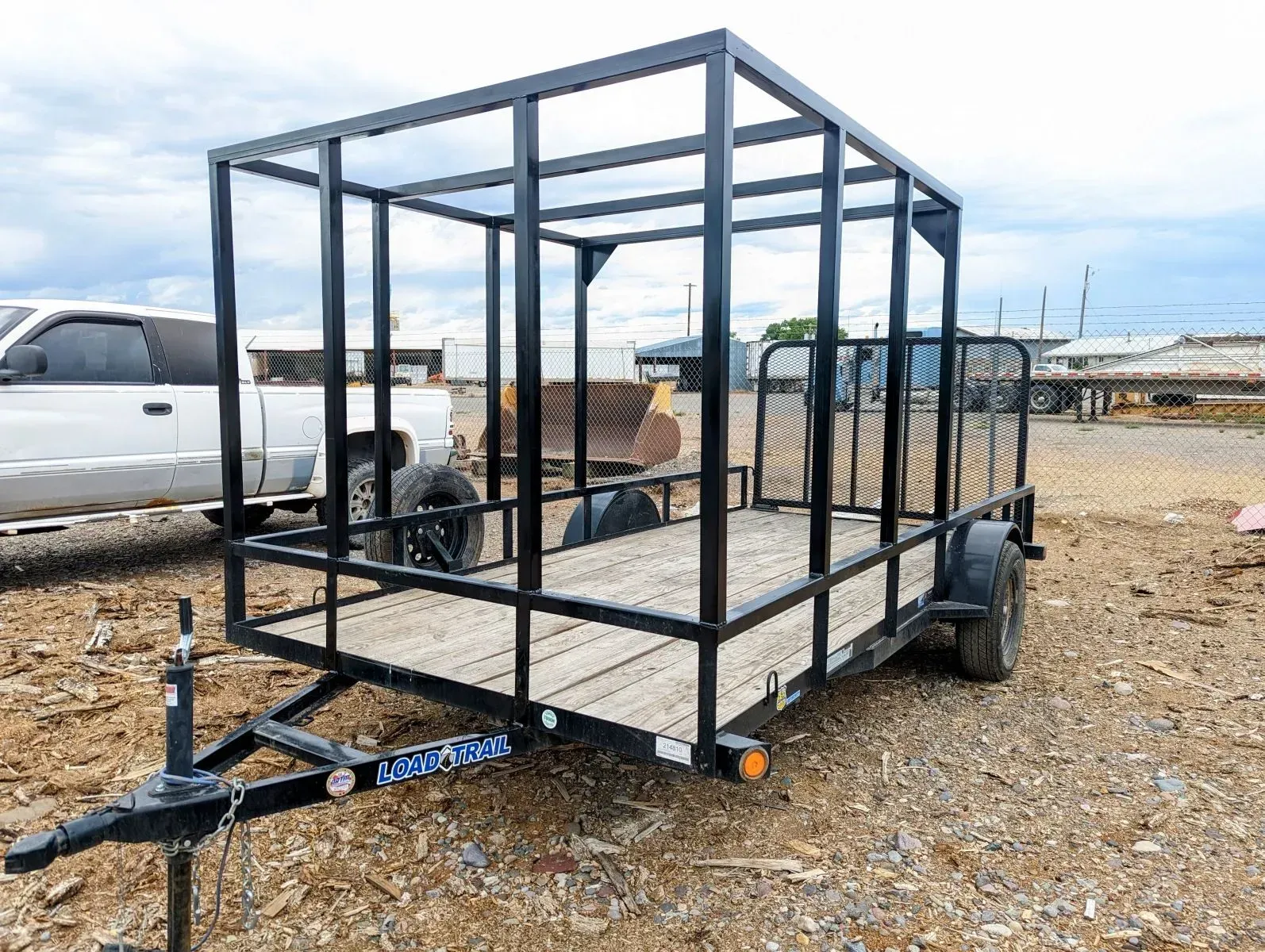 Black utility trailer with a metal frame parked on gravel in an outdoor lot