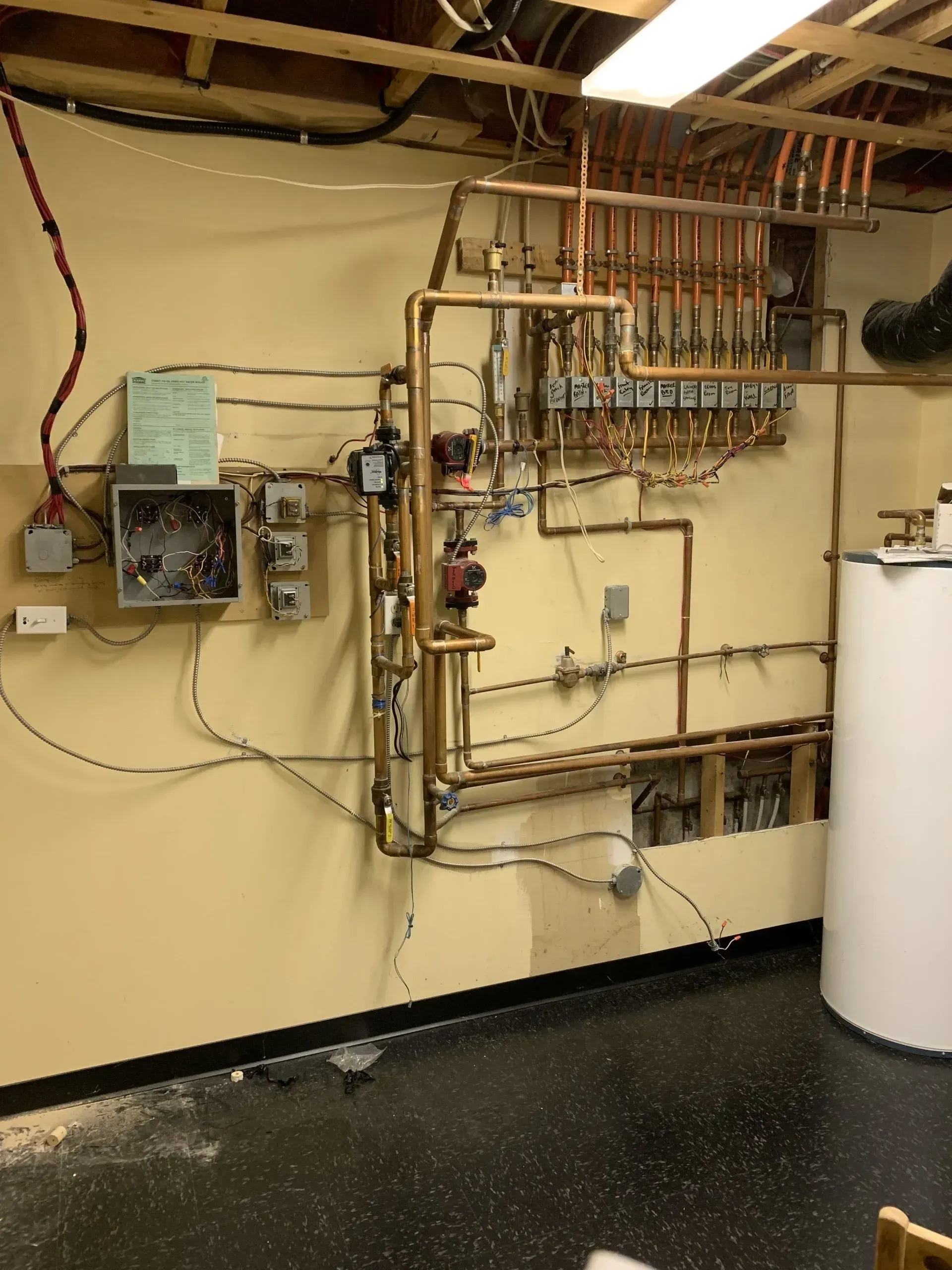 Copper pipes and wiring on a tan wall in a utility room next to a water heater.