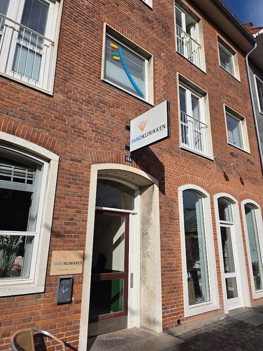 Tandkliniklokale med stol, loftslampe og stort vindue med udsigt over murstensbygninger