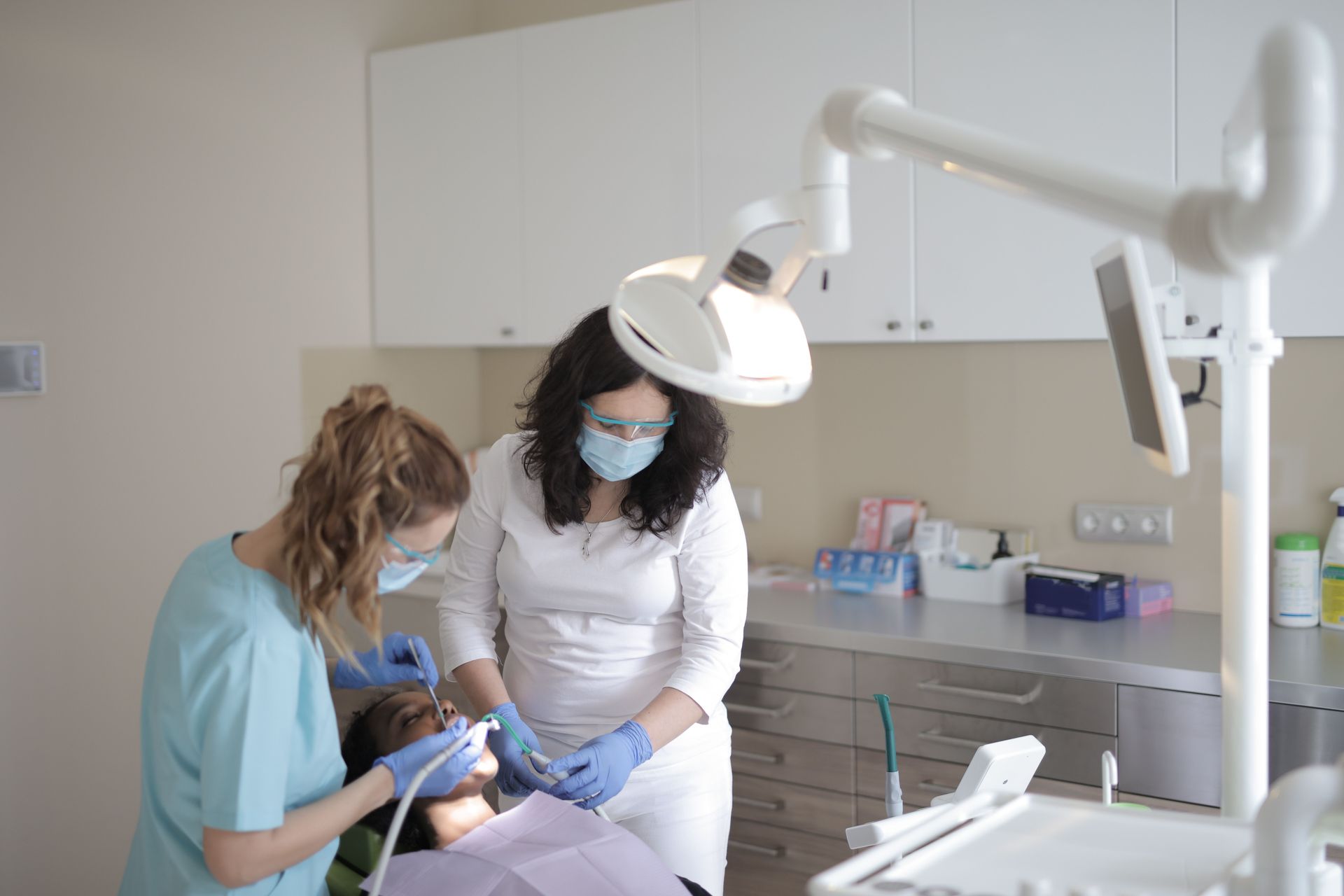 To tandlæger i en lys klinik undersøger en siddende patient under en tandlampe