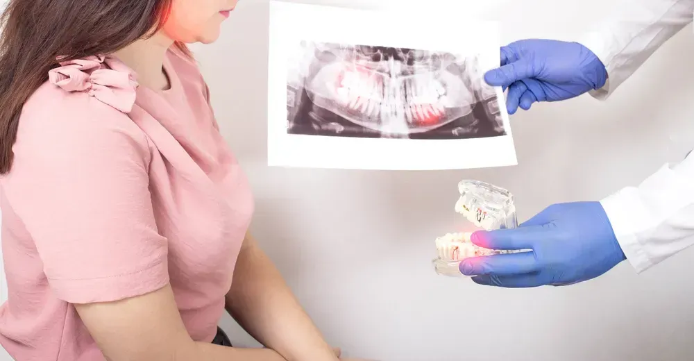 Tandlæge viser patienten et røntgenbillede af tænderne og en model af tænderne.