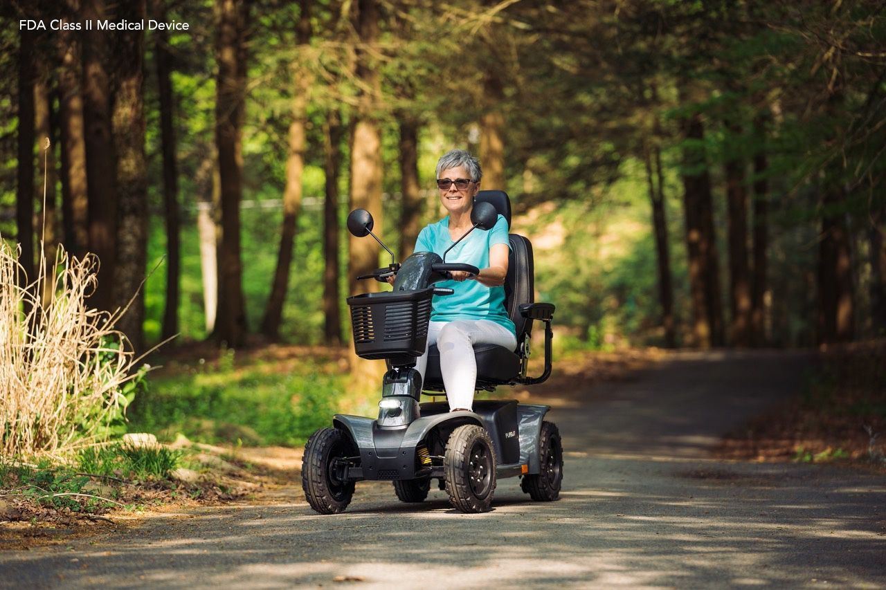 Woman on a motorized scooter on a wooded path, smiling.