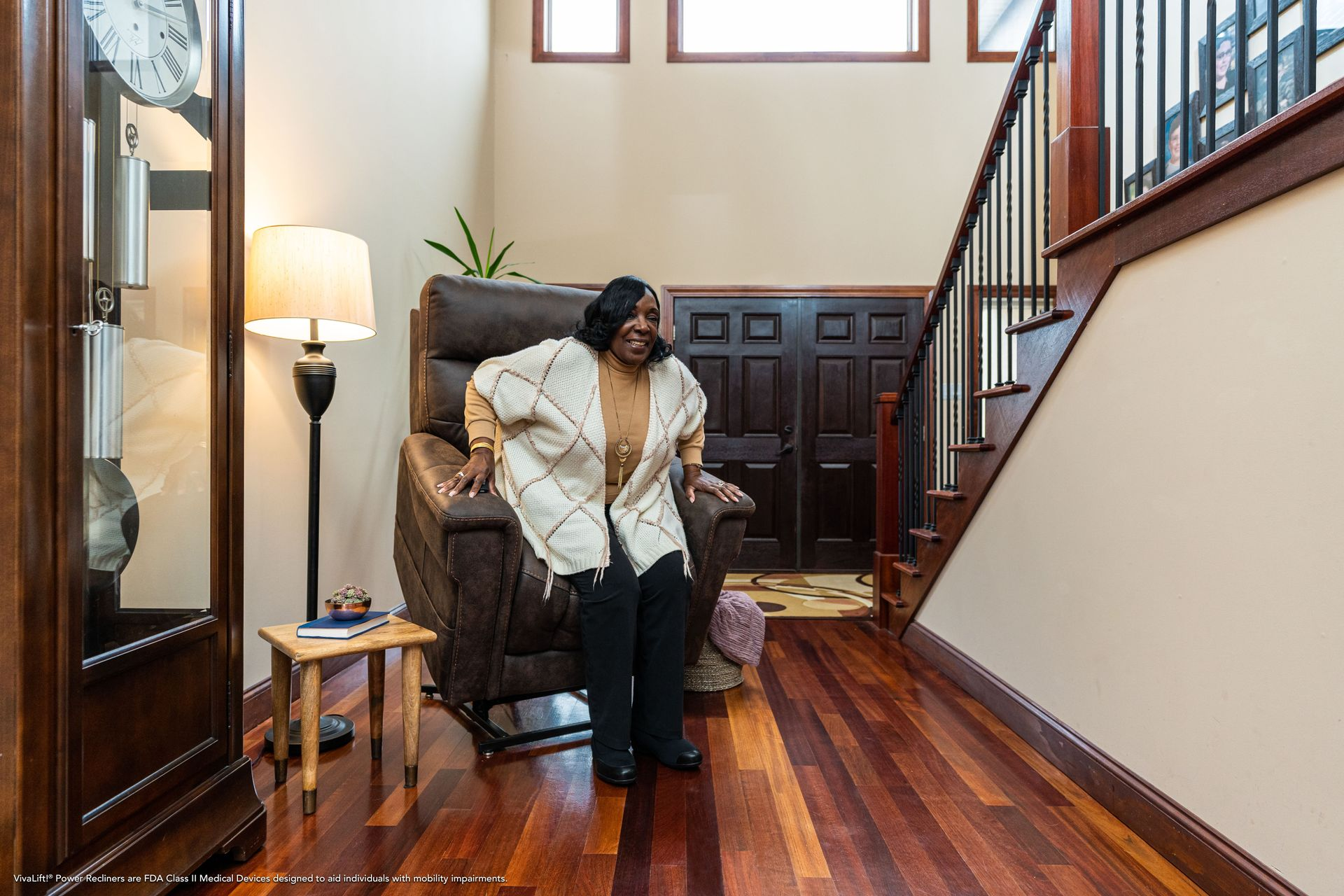 Woman standing up from a lift chair in a home's entryway with wooden floors and staircase.
