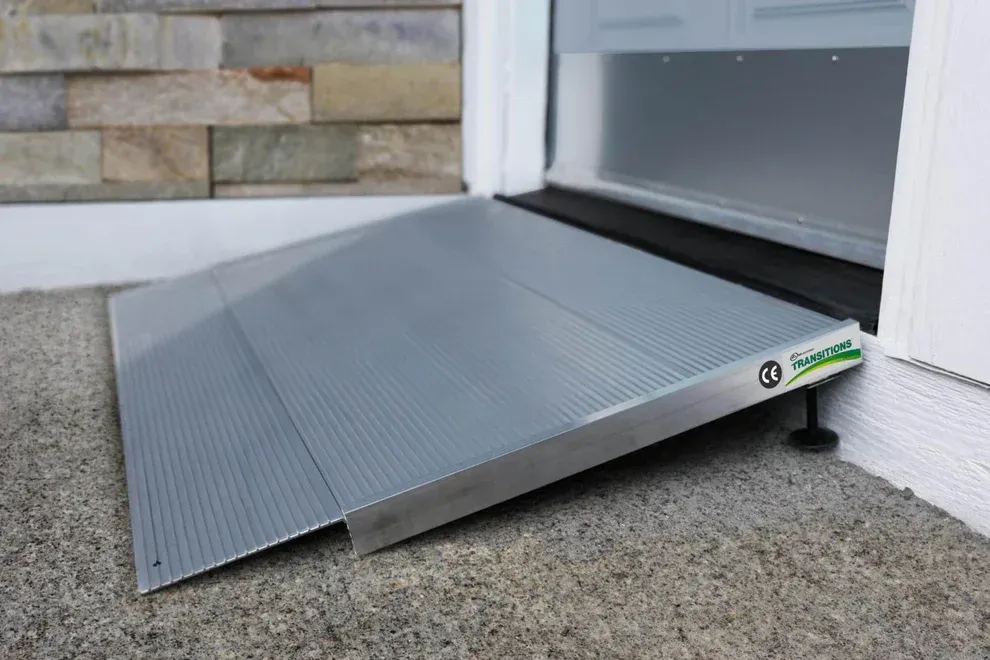 A portable, ribbed metal wheelchair ramp positioned at a doorway entrance to provide accessible entry.
