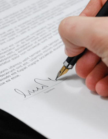 Hand signing a document with a pen on white paper