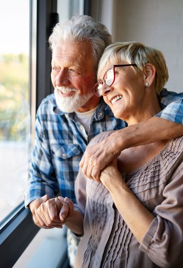 Smiling couple by a window, leaning close and holding hands in soft natural light