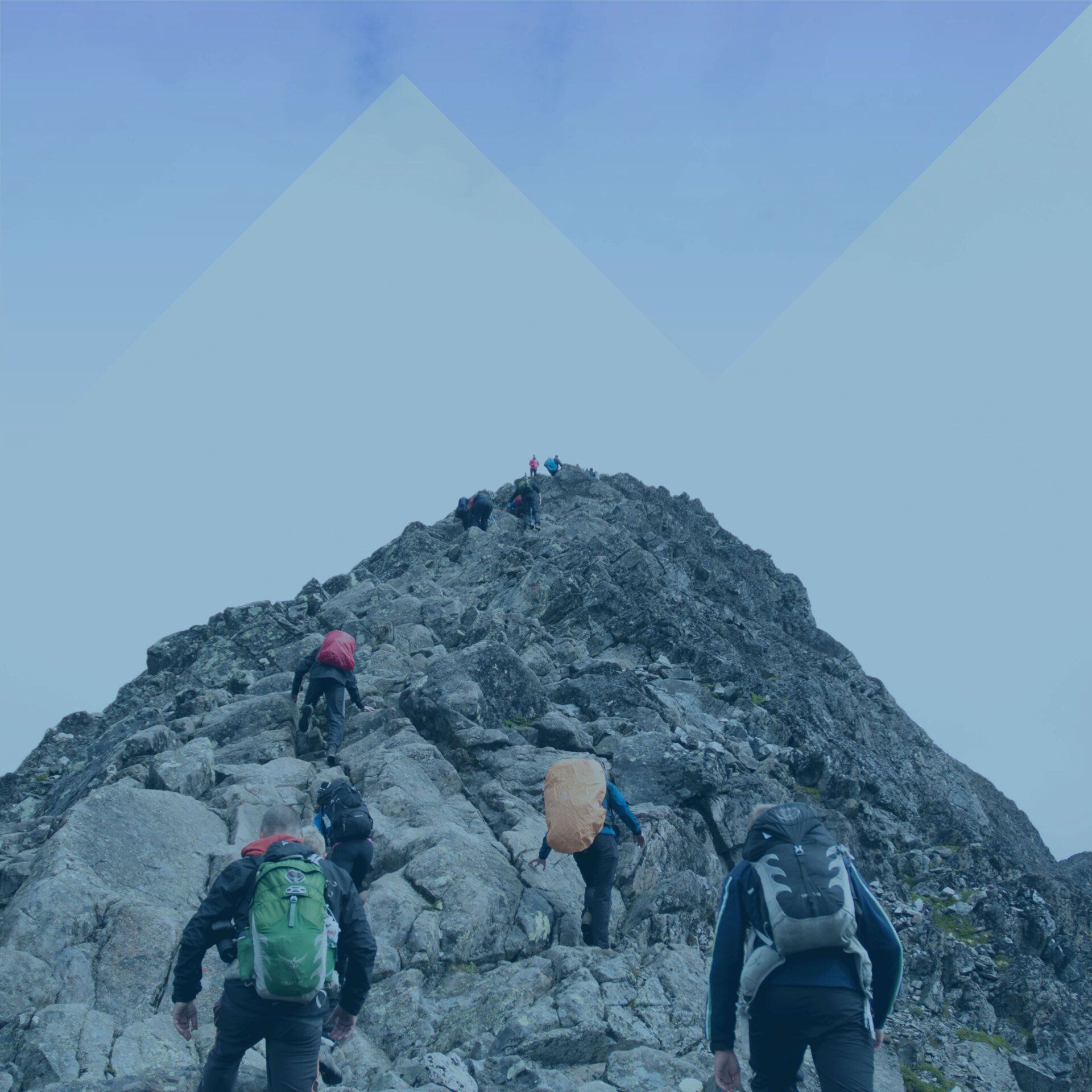 Hikers climbing a steep rocky mountain trail under a blue sky.