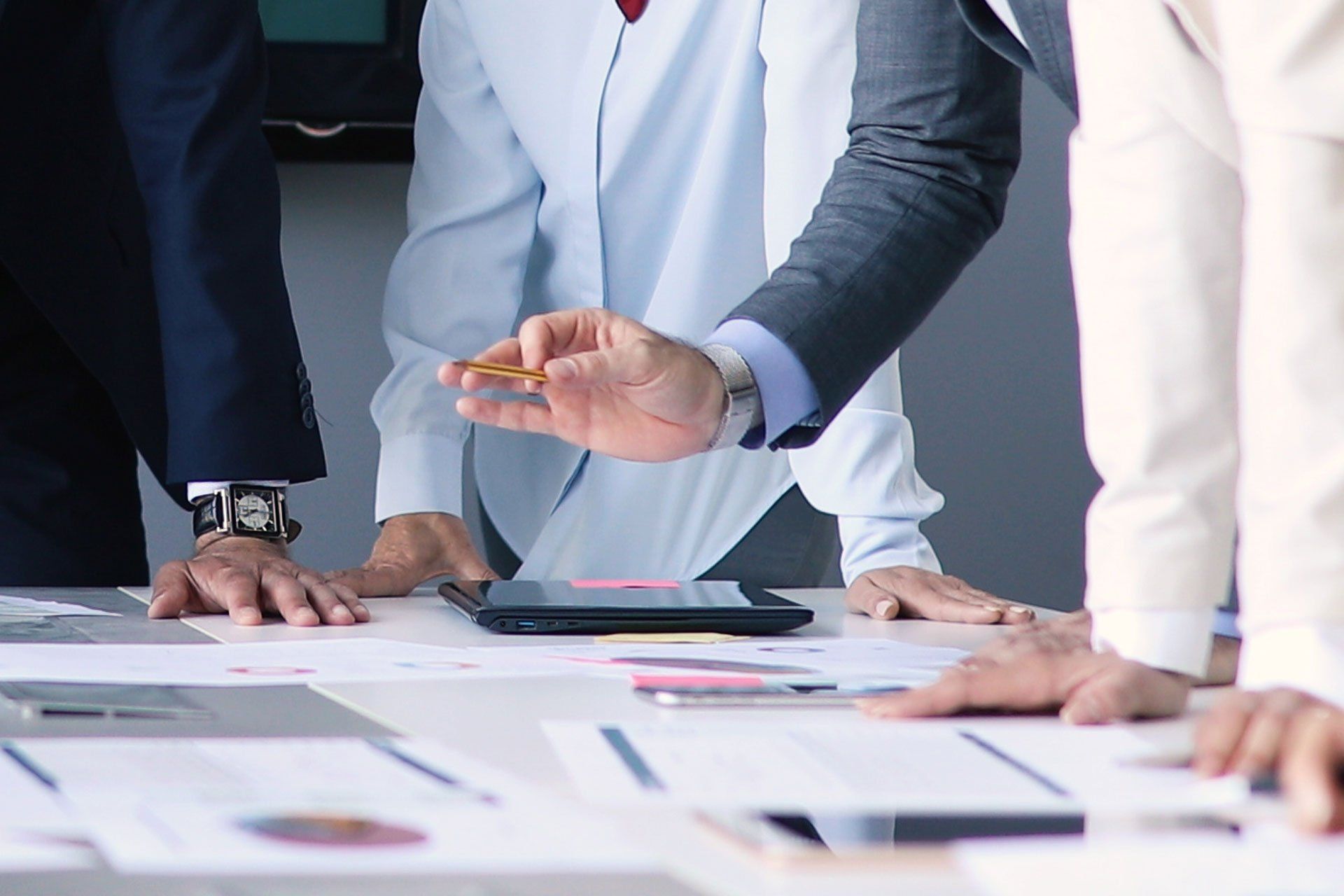 People in business attire discussing documents around a conference table, one gesturing over papers