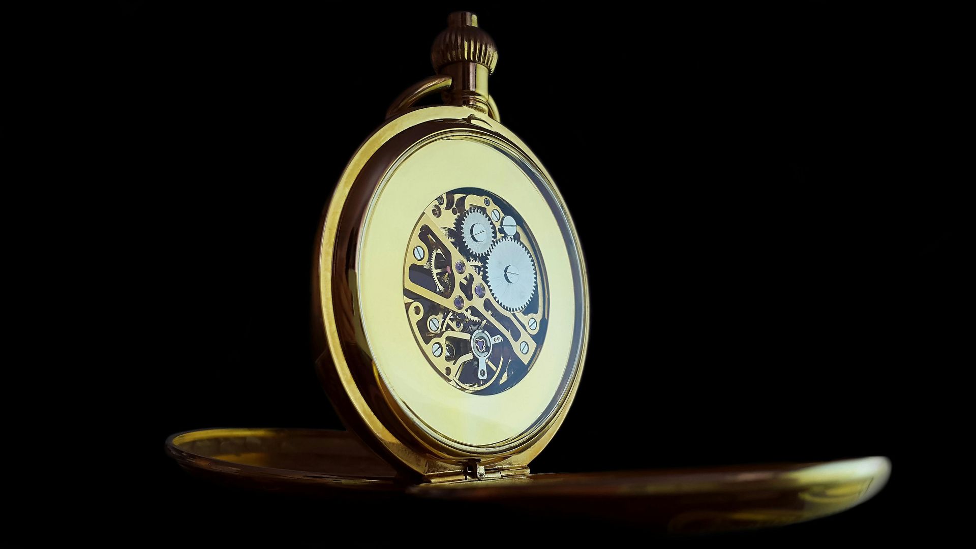 Open pocket watch with gold case and blue face, standing on a dark surface against a black background