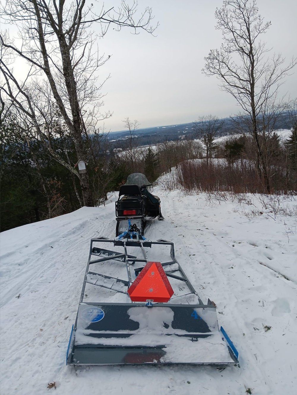 A snowmobile is pulling a trailer down a snowy road