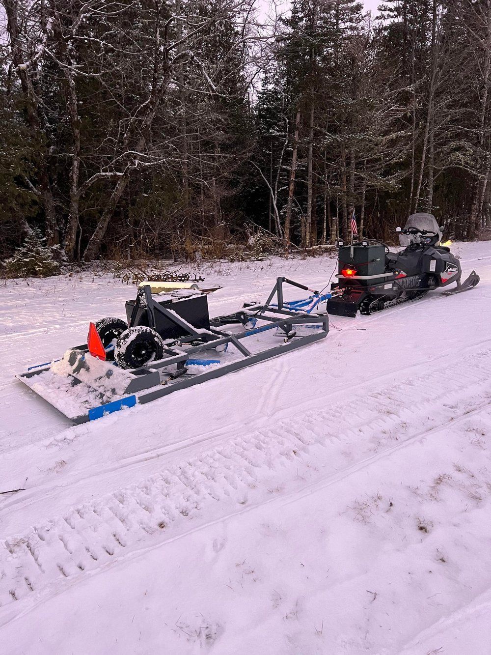 A snowmobile is pulling a sled down a snowy road.
