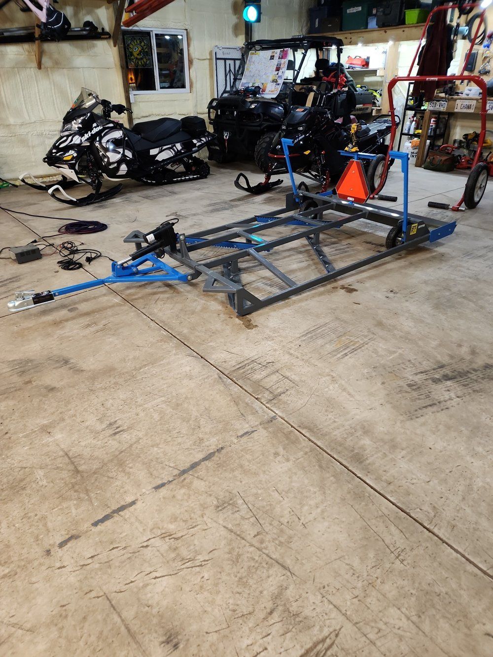 A snowmobile trailer is sitting in a garage next to a snowmobile.