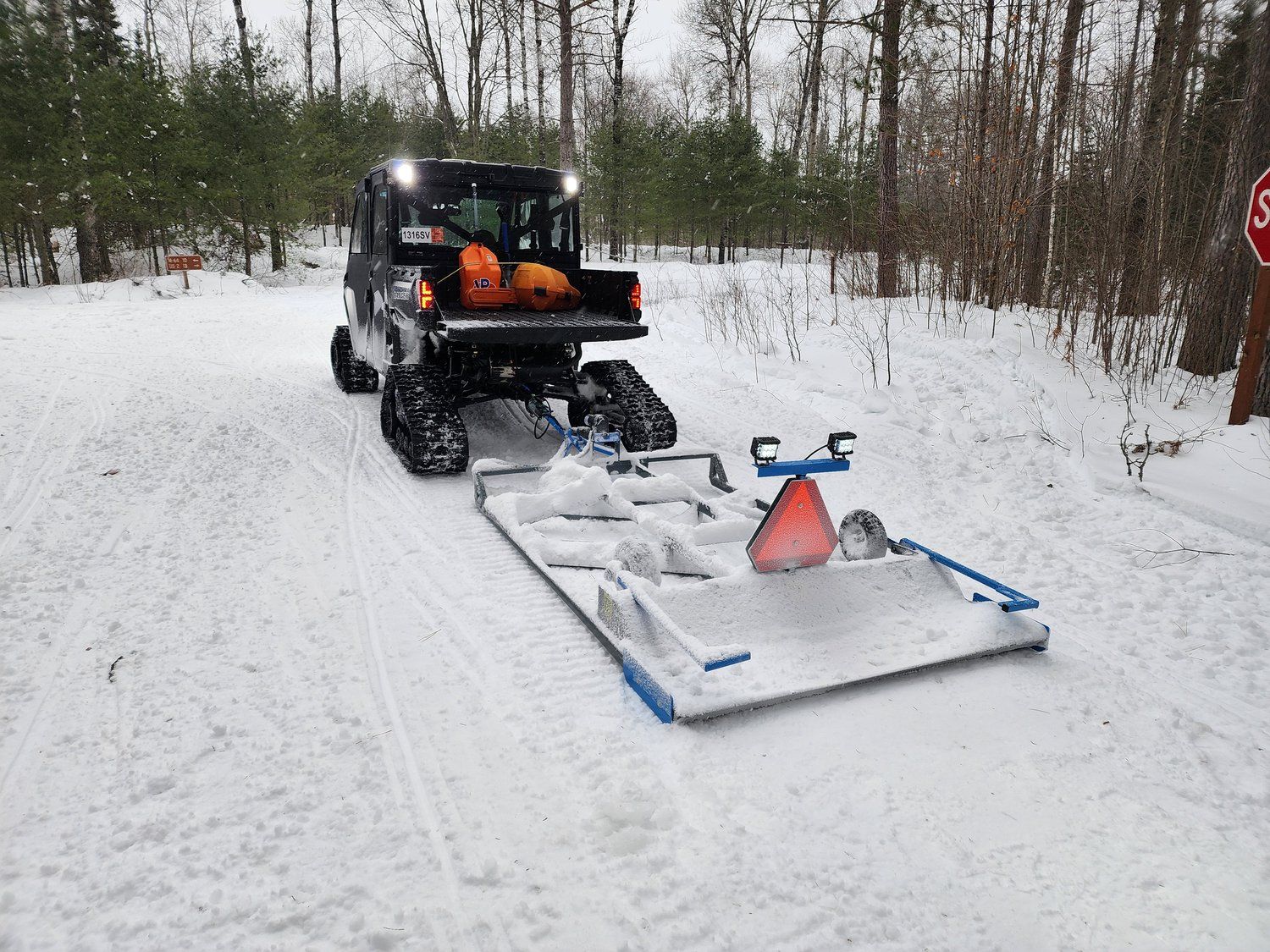 A snowmobile is driving down a snowy road next to a stop sign.
