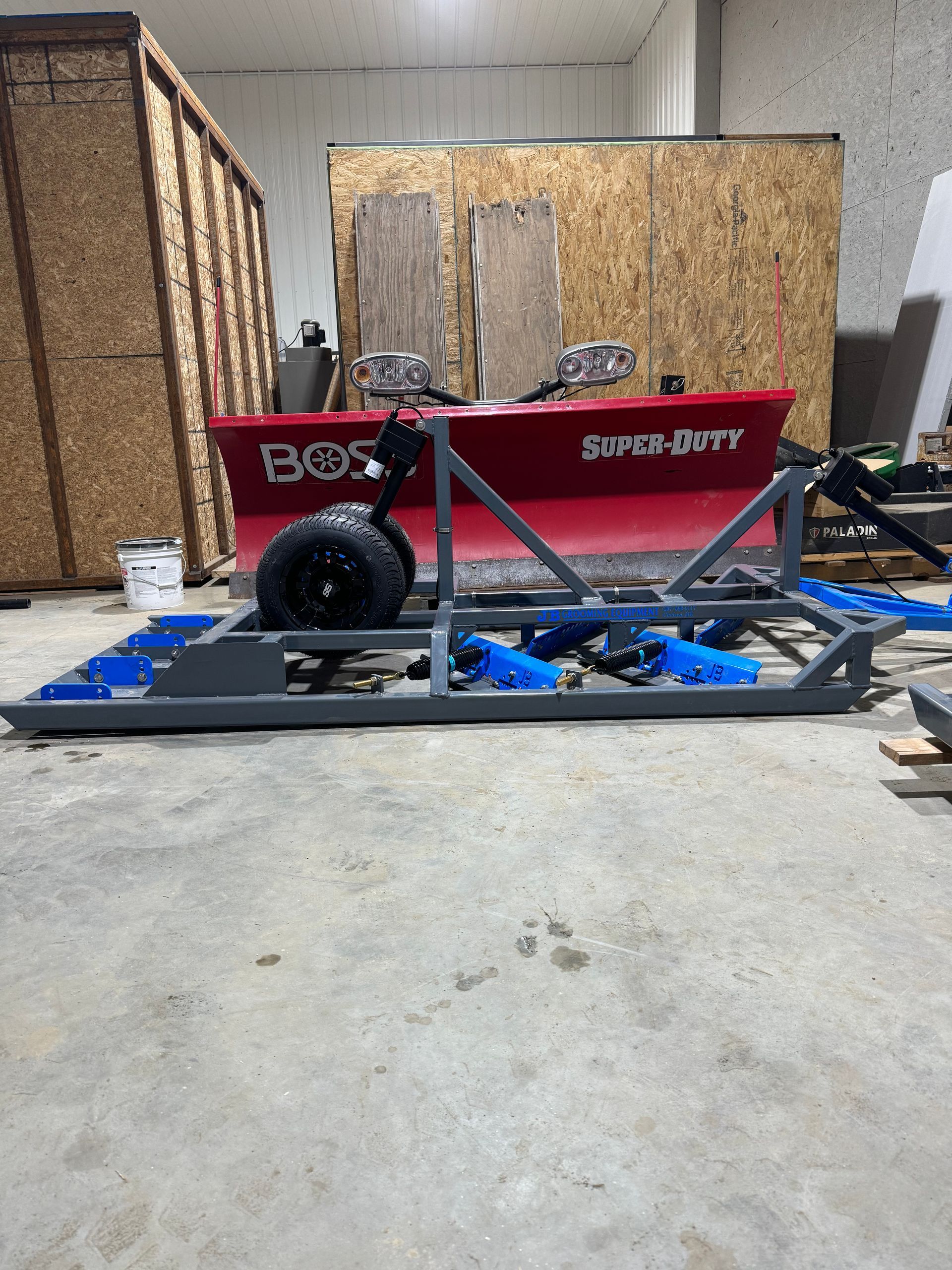 A snow plow is sitting on the ground in a garage.