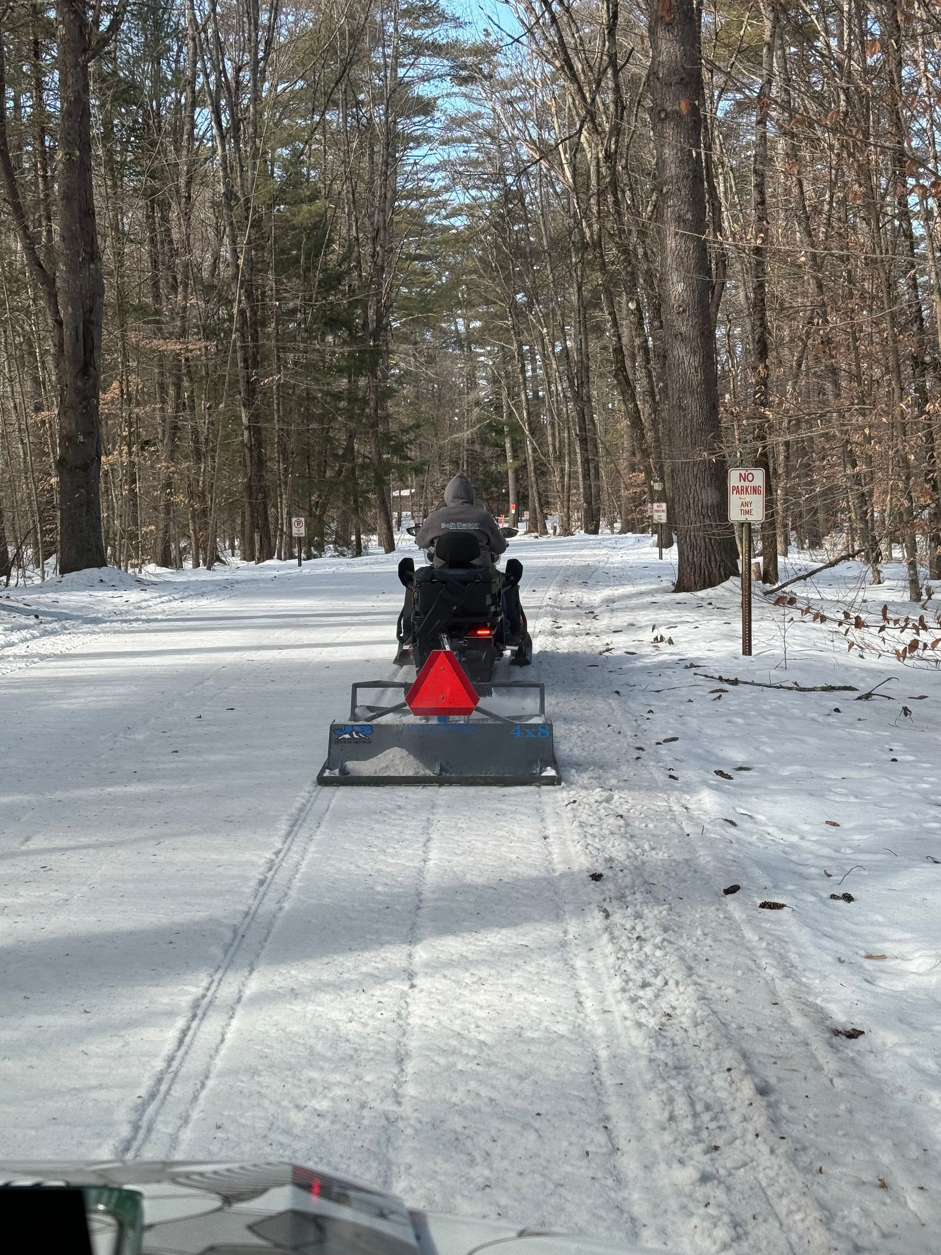 A snowmobile is driving down a snowy road in the woods
