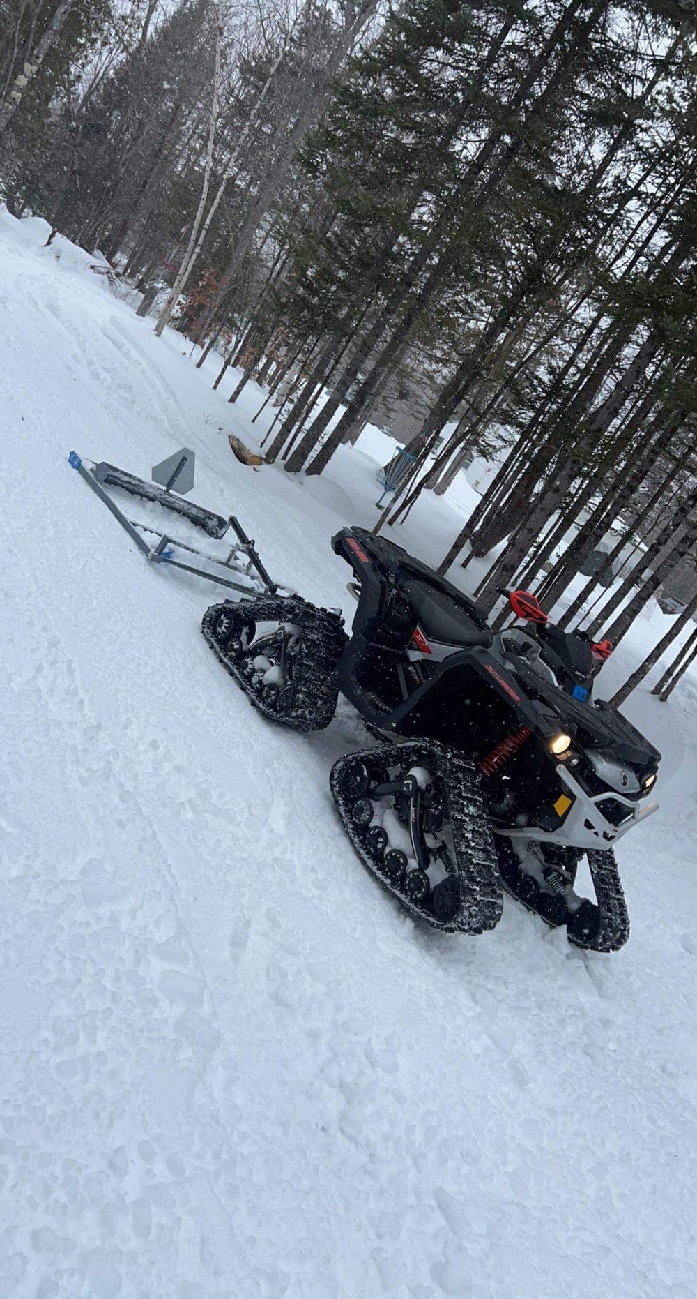 A person is riding an atv in the snow with a sled attached to it.