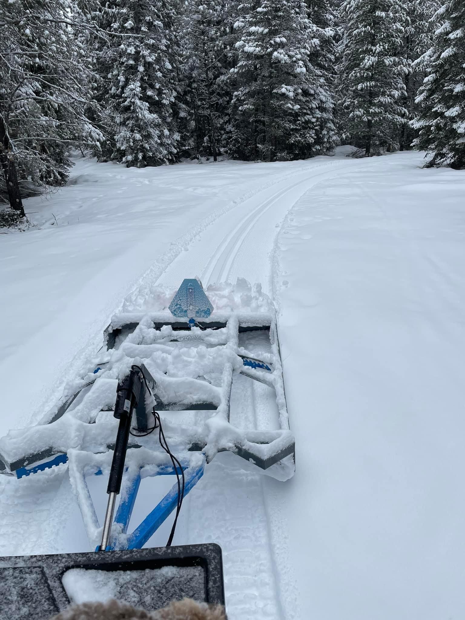 A snowmobile is driving down a snowy road in the woods.