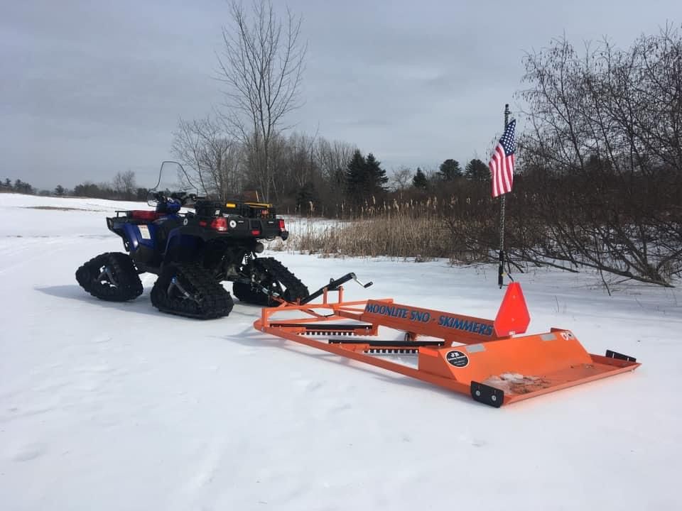 An atv is parked in the snow next to a trailer.