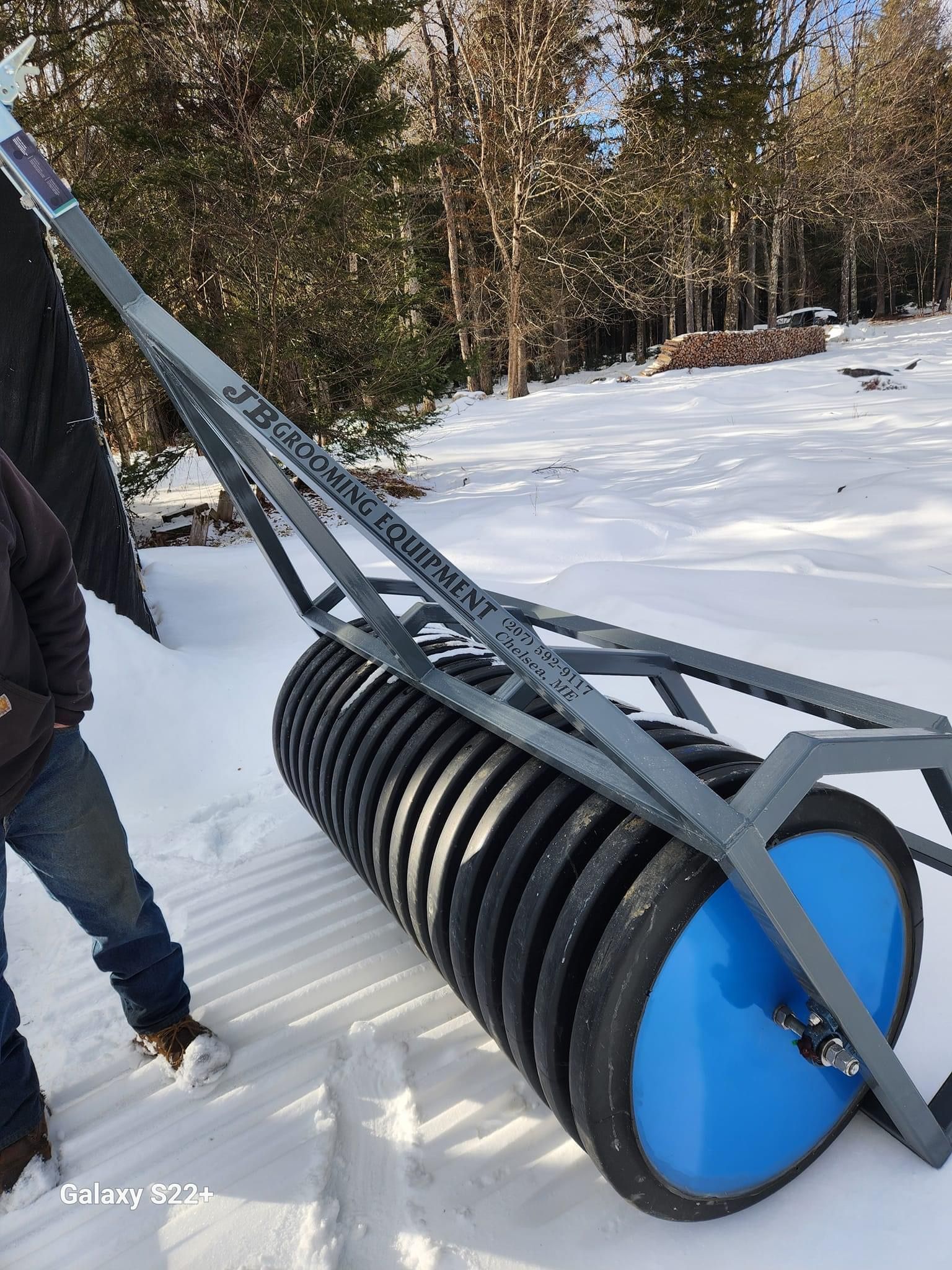 A person is standing next to a large roller in the snow.