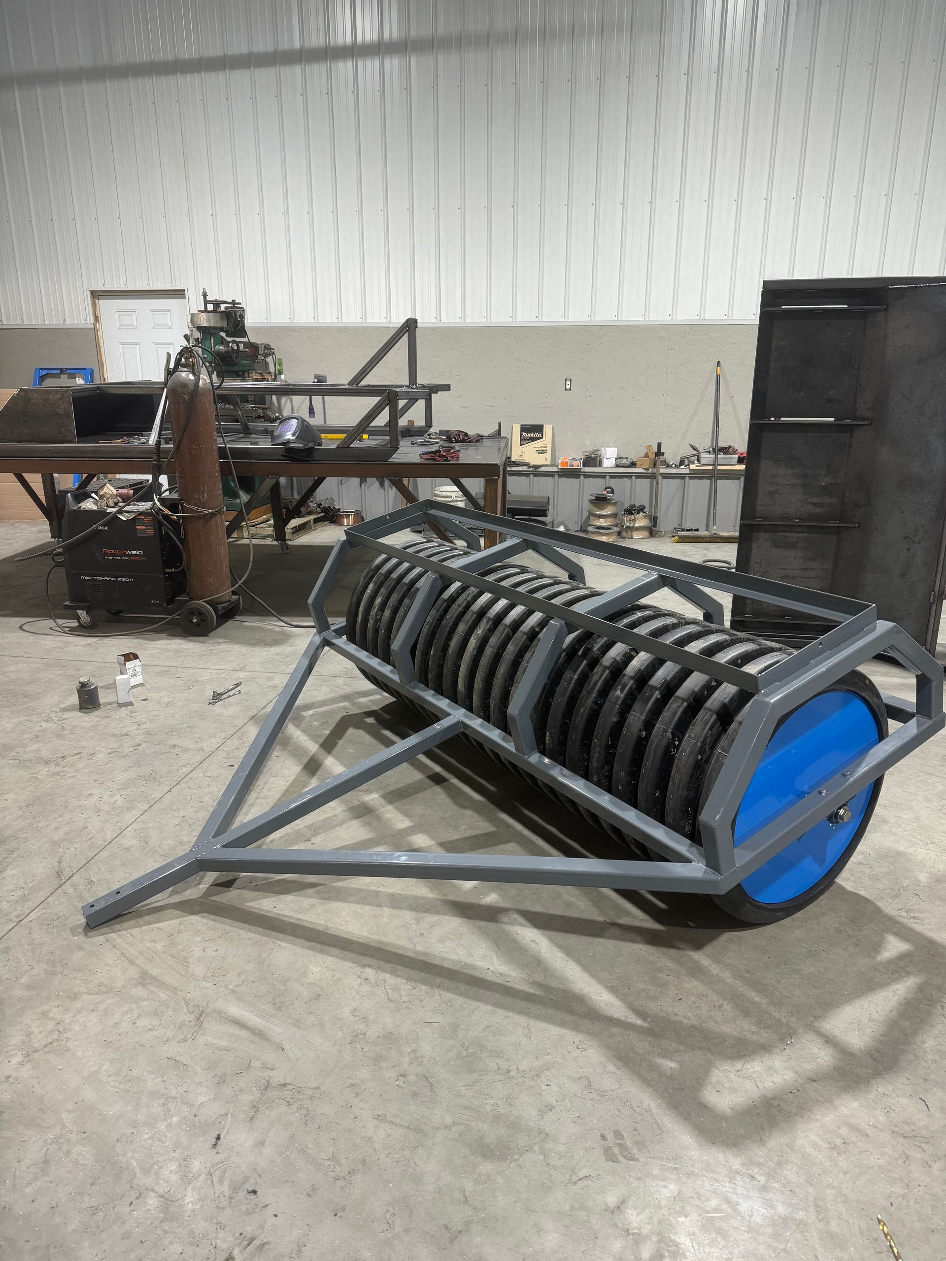 A large metal roller with a blue wheel is sitting in a warehouse.
