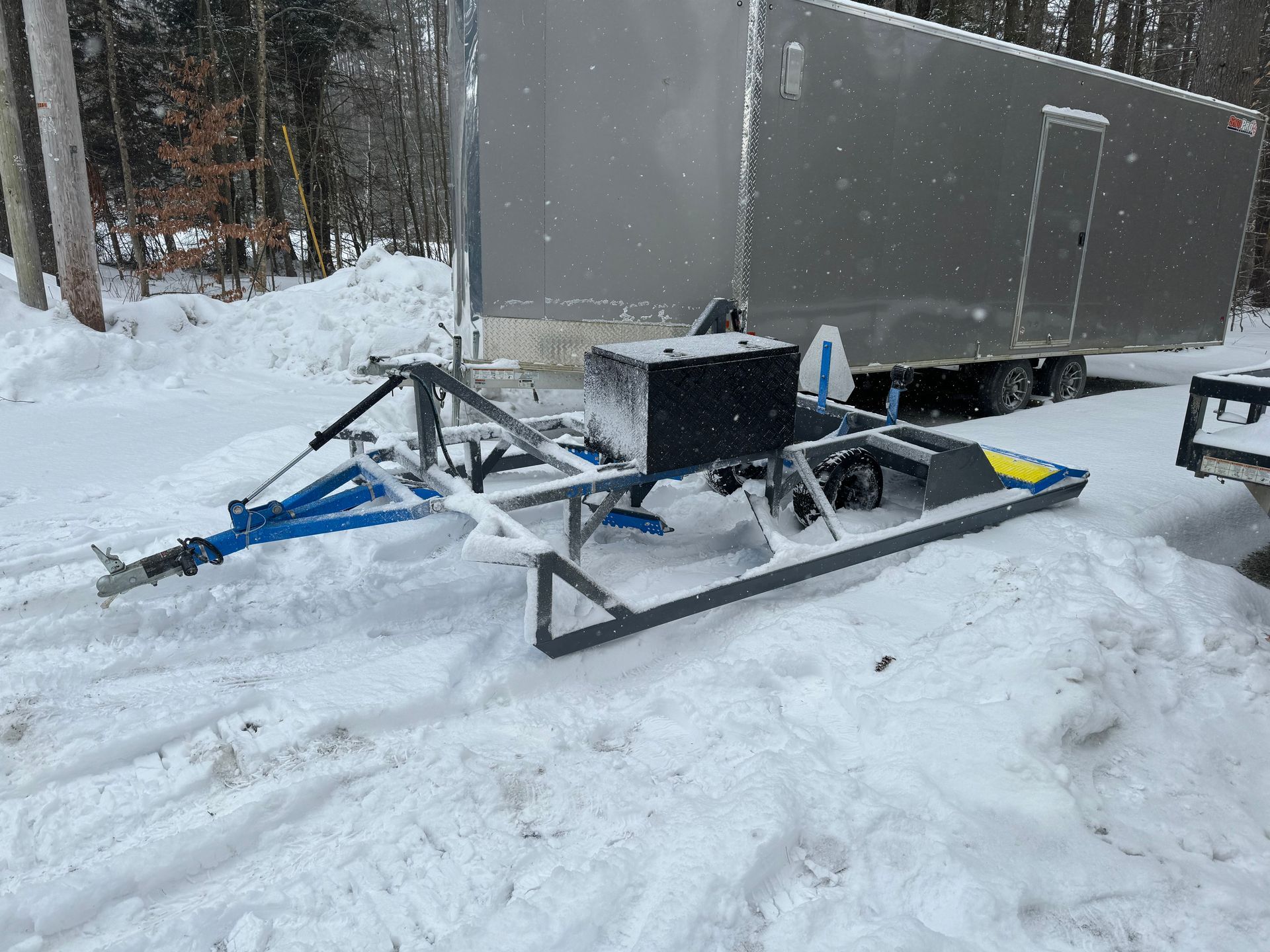 A snowmobile is parked in the snow next to a trailer.