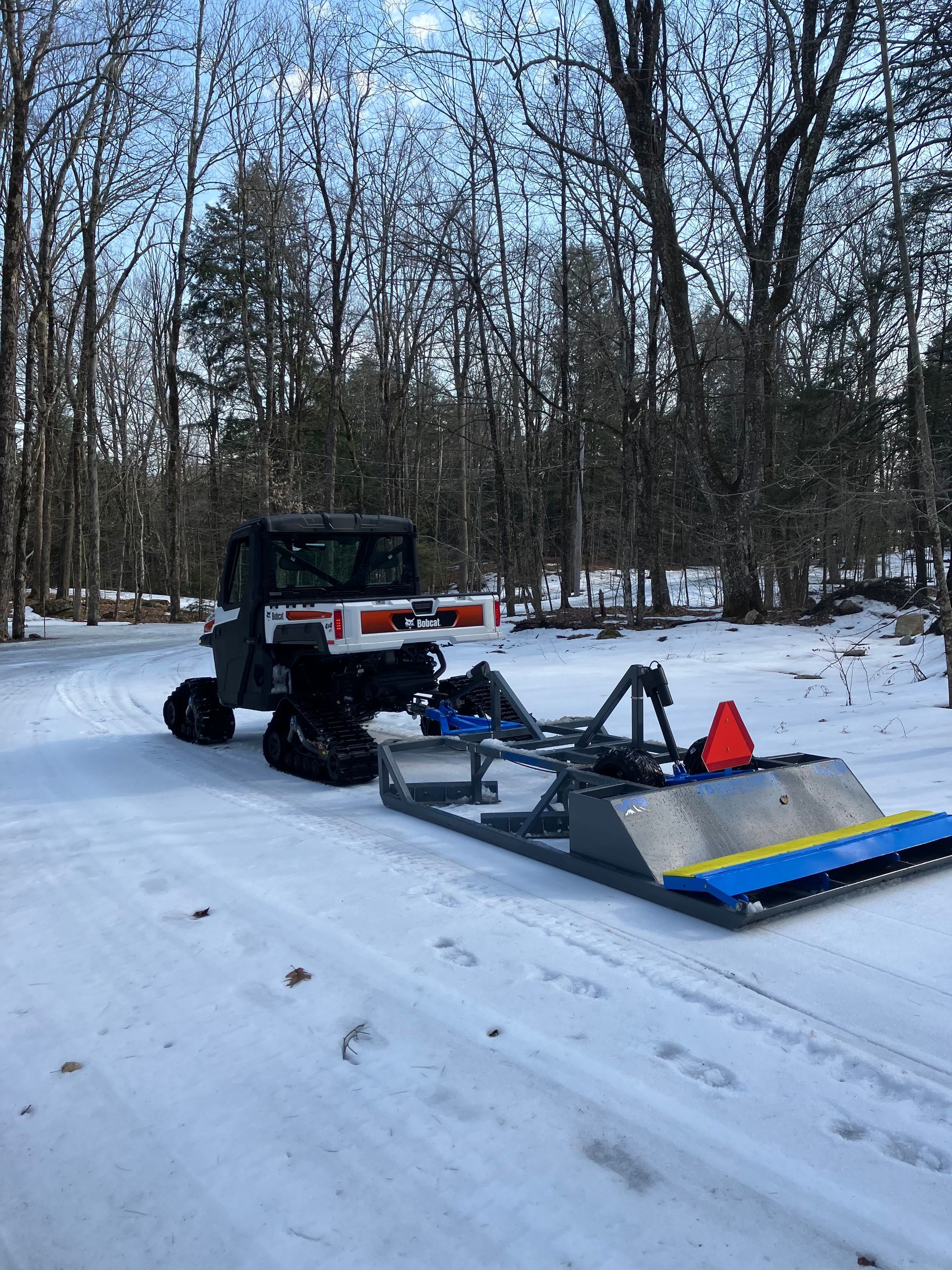 A snowmobile is parked in the snow with a plow attached to it.