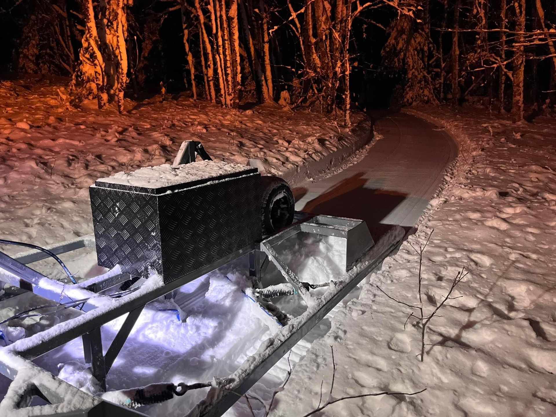 A snowmobile is parked on a snowy road at night.