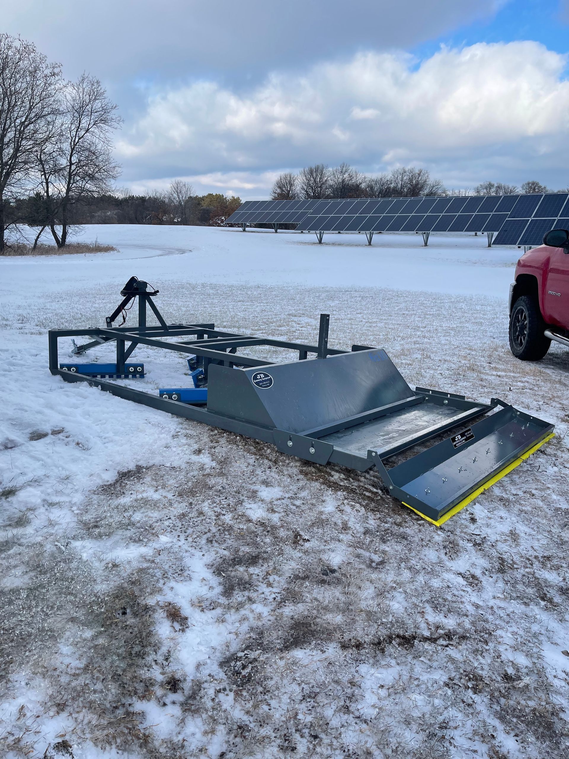 A red truck is parked in the snow in front of a field of solar panels.