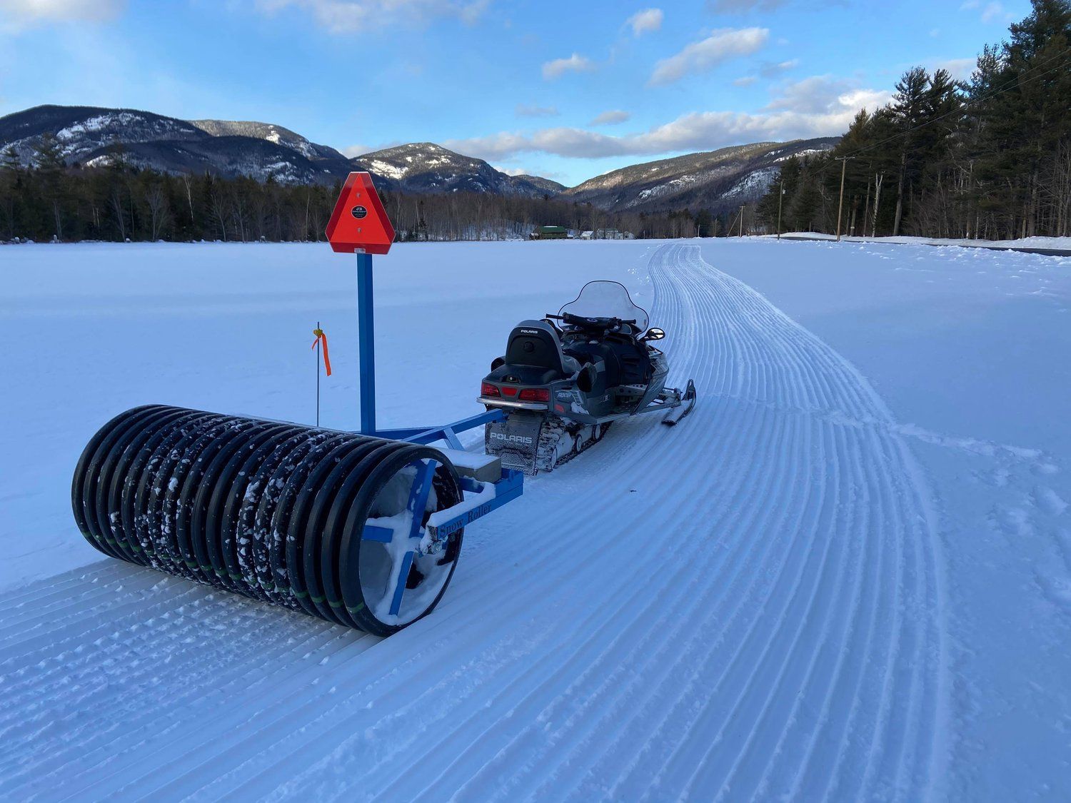 A snowmobile is pulled by a roller in the snow.