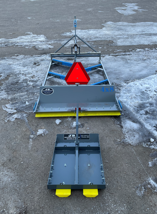 Two gray and yellow ice-grooming machines on a snow-covered paved surface.