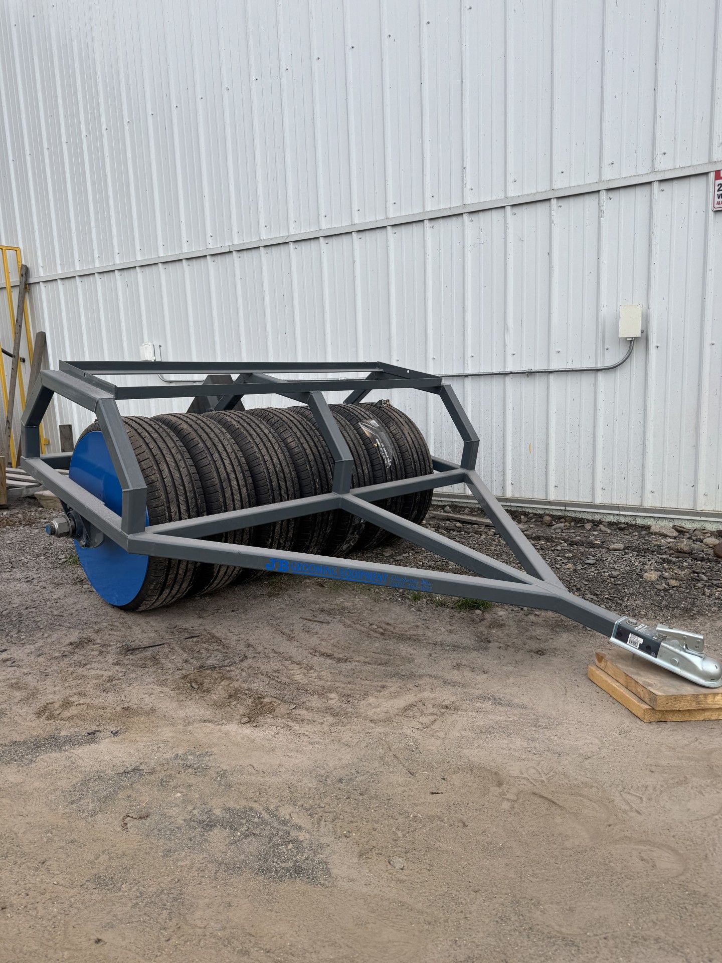 Gray and blue tire roller on a trailer, used for ground compaction.