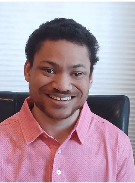 Smiling person in a pink button-up shirt seated indoors against a light background
