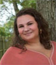 Smiling woman in a coral top leaning against a tree outdoors