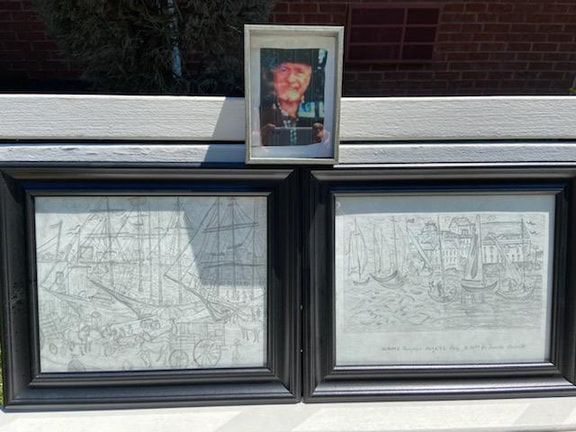 Framed memorial portraits and drawings in a window, with a small color photo centered above them