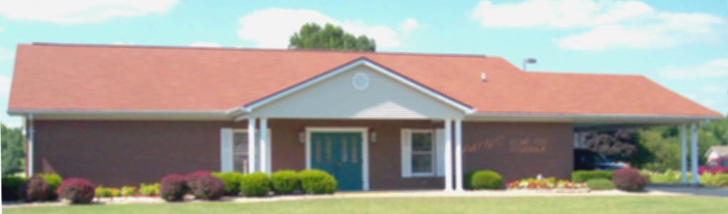 Single-story brick building with red roof and white columns, viewed from the front on a sunny day