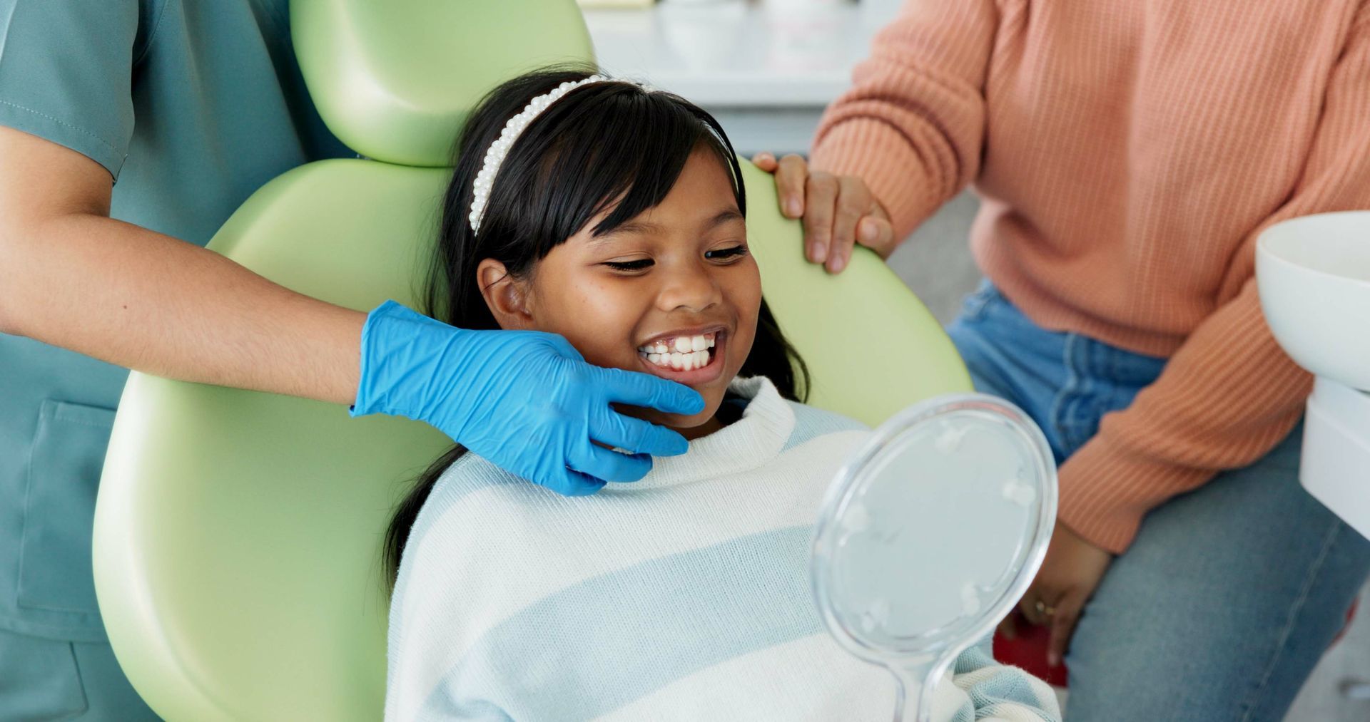 Dental professional supporting a child in a dental chair while a caregiver stands nearby. Dental professional supporting a child in a dental chair while a caregiver stands nearby.