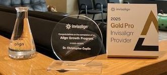 Invisalign award, clear glass beaker and plaque on a wooden surface. The plaque says,