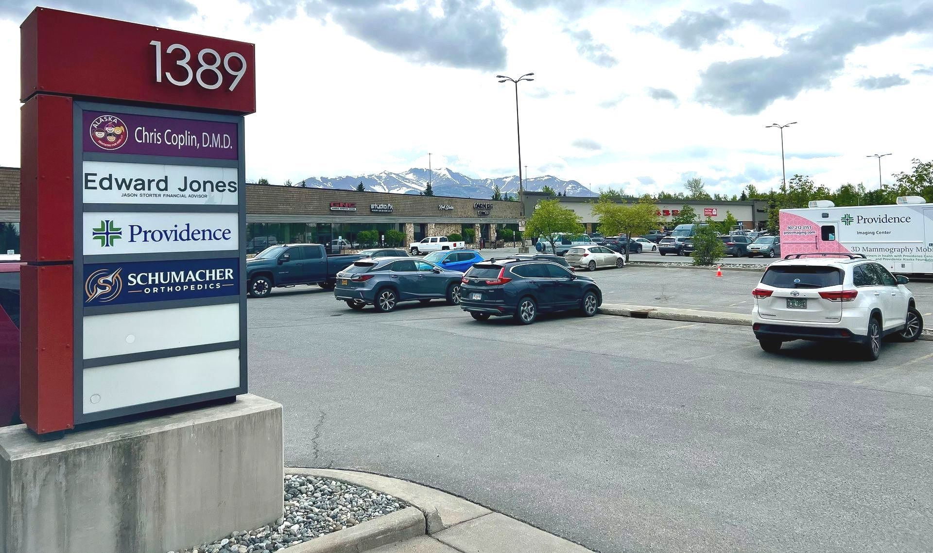 Sign for businesses, 1389, with parking lot and mountain backdrop.