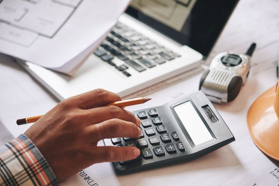 A person is using a calculator in front of a laptop.