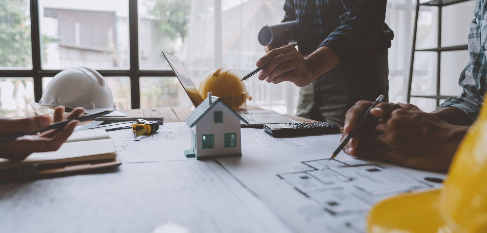 A group of people are sitting at a table with a model house and hard hats.