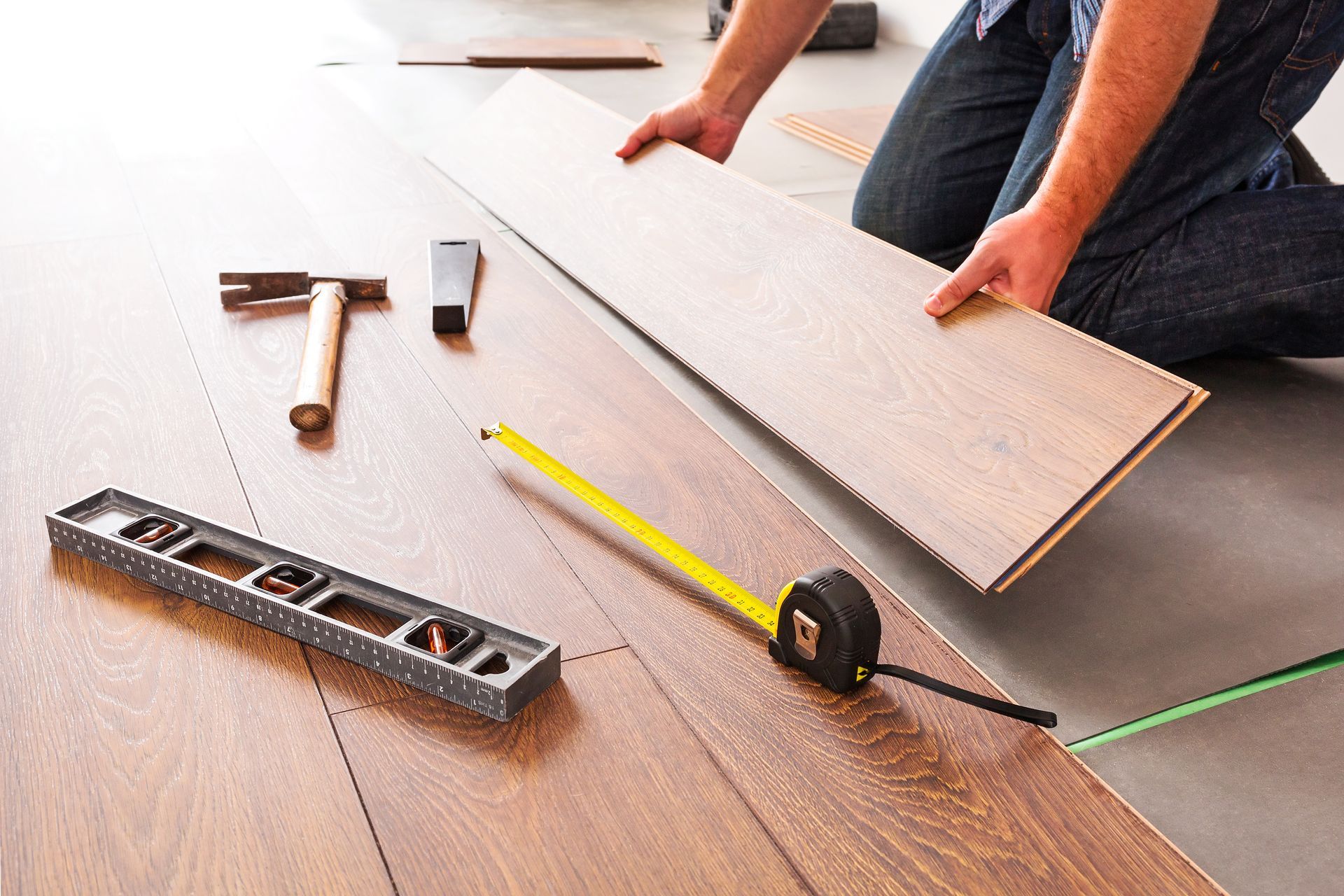 A man is kneeling down to install a wooden floor.