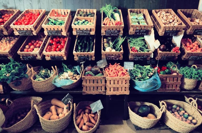 A variety of fruits and vegetables are displayed in baskets on a shelf.