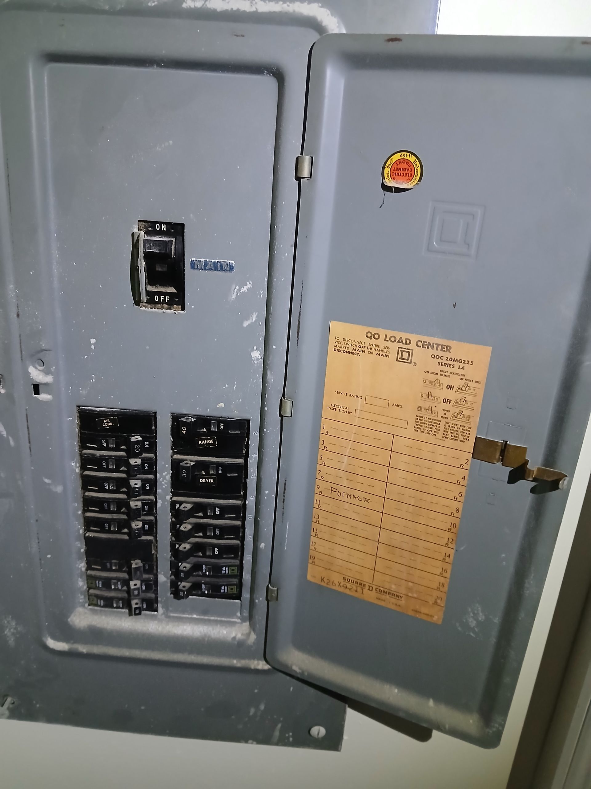 Electrical panel with open door, breakers visible. Gray metal box, a label inside door.