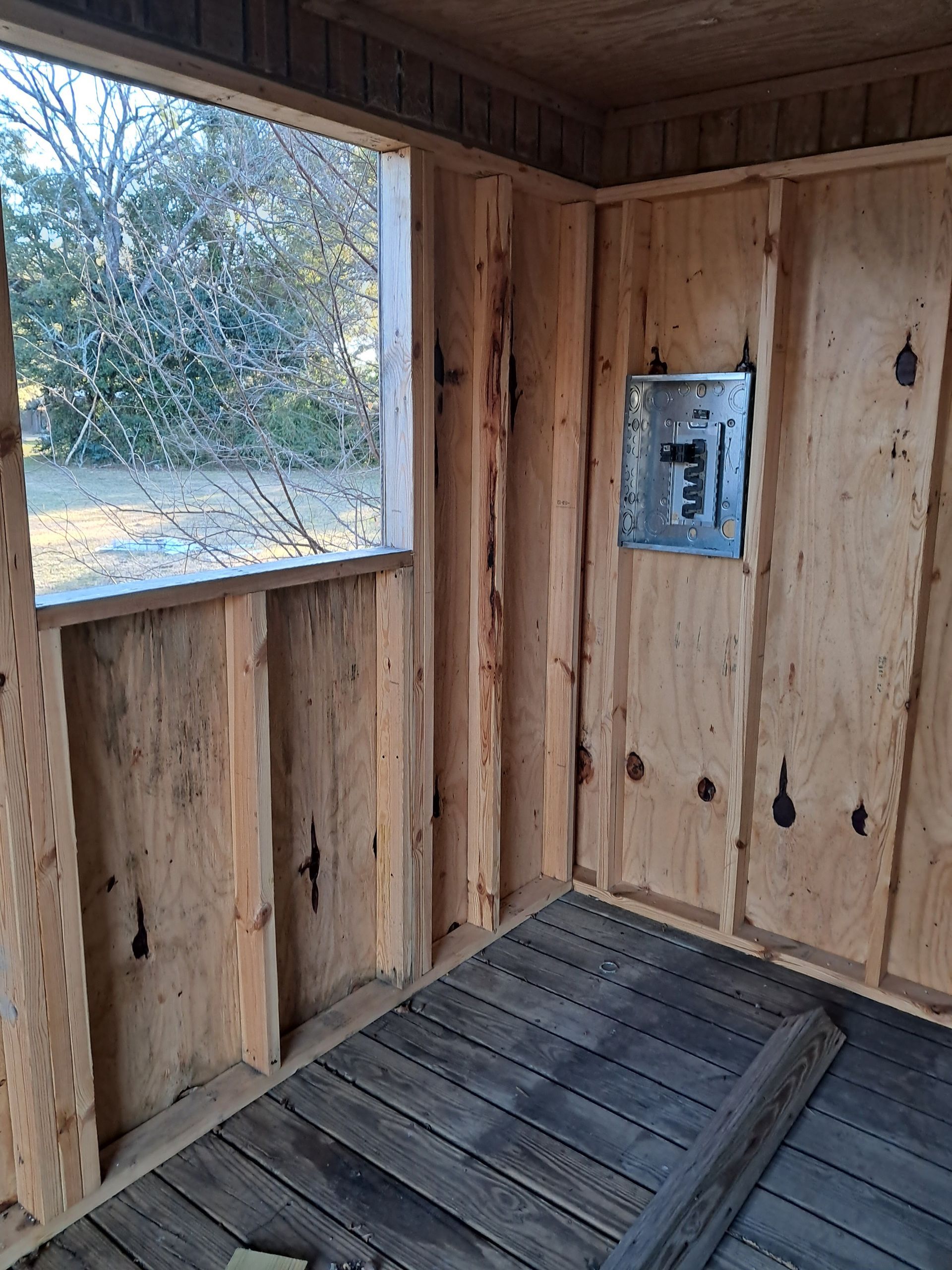 Interior of a small wooden structure with a window and electrical panel.